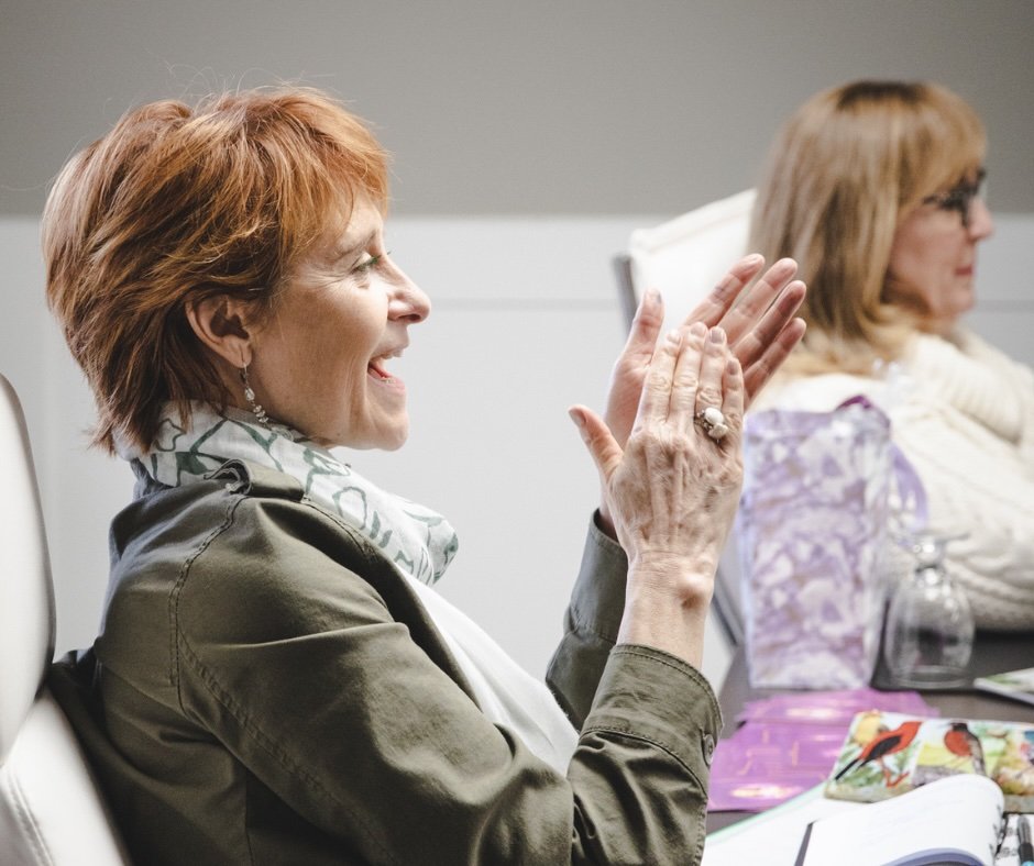 A woman with short red hair clapping and smiling during a business meeting.